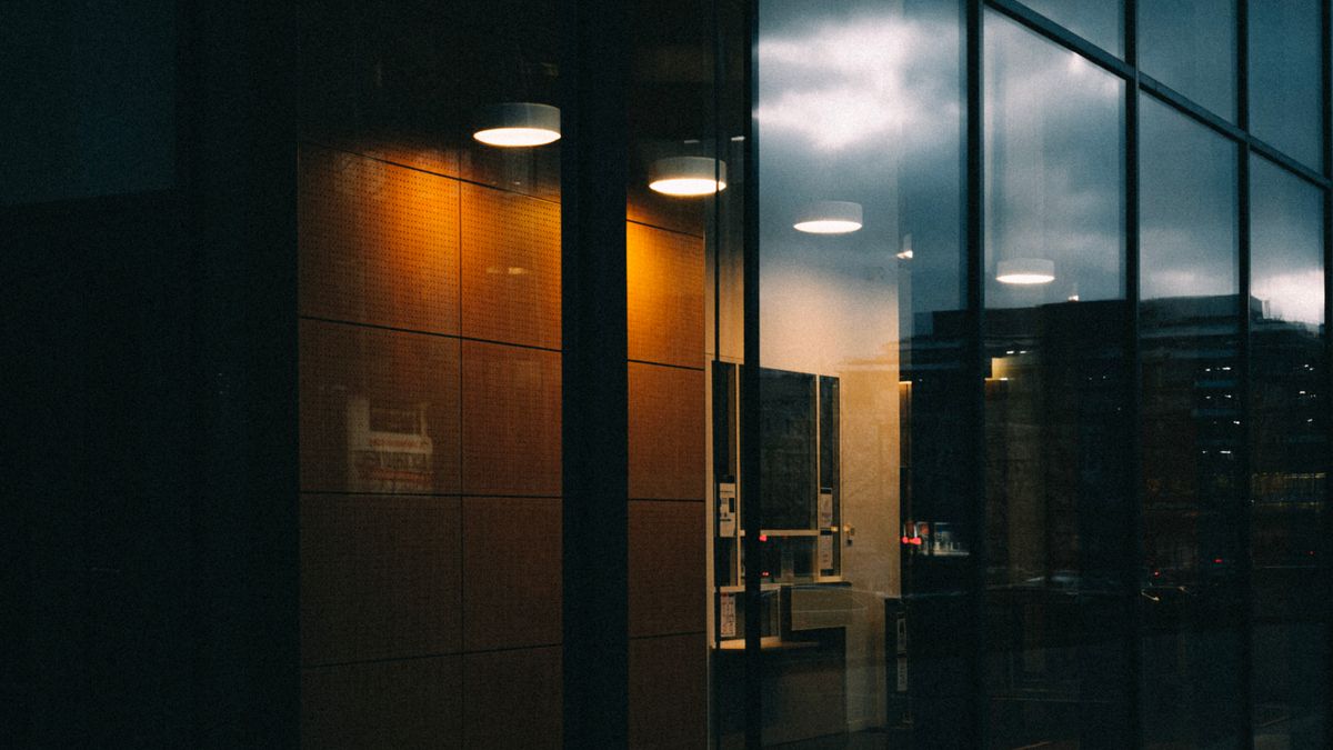 Modern building with warm interior lights and evening sky reflections on its glass facade, showing reflection refraction and diffraction of light