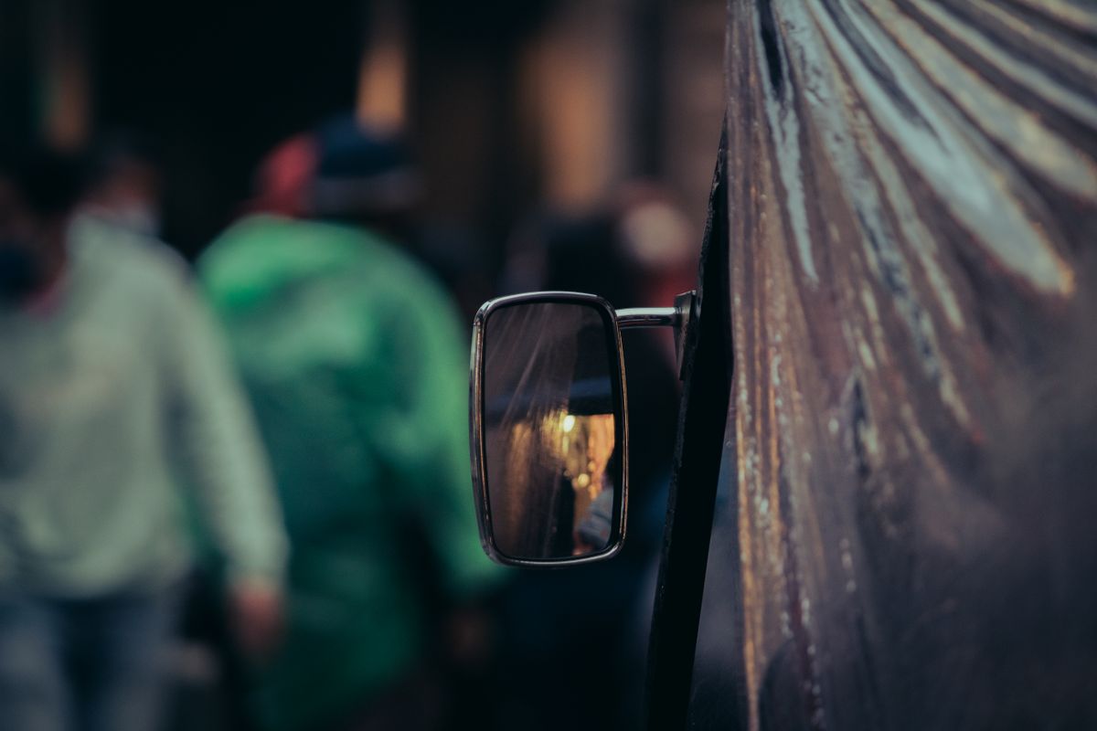 A close-up view of an urban street scene reflecting in a vehicle's convex side mirror, showing a diminished virtual image of the street behind