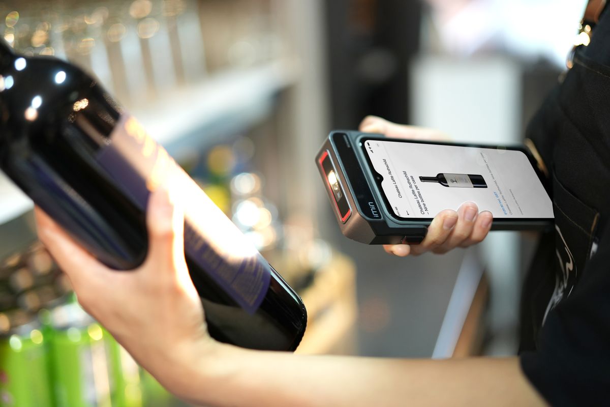 Close-up of a person scanning a wine bottle with a portable barcode scanner in a store, showing laser technology in retail