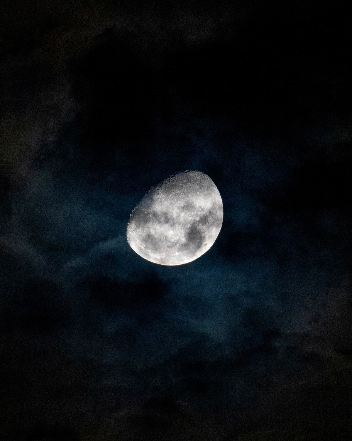Gibbous moon shining through clouds, demonstrating what is reflective light as sunlight bounces off the moon's surface