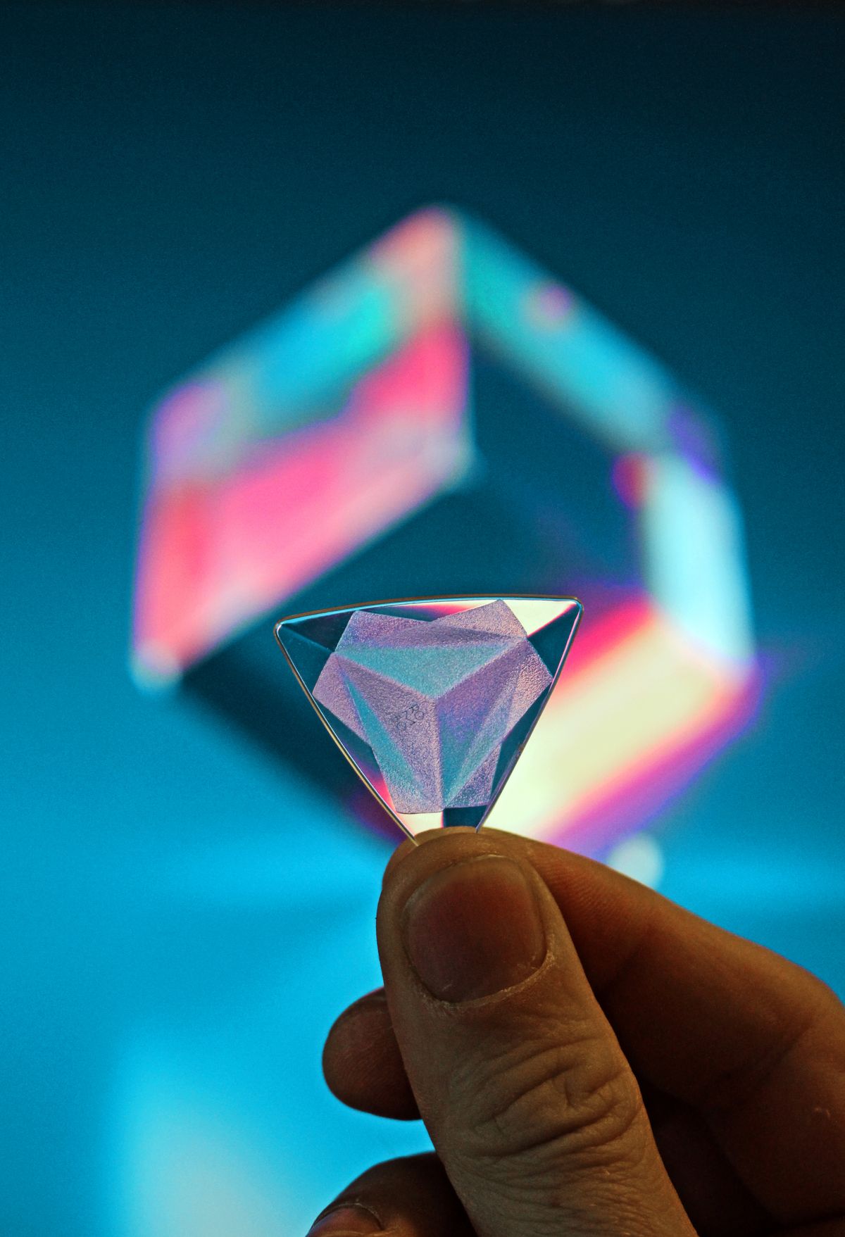 Glass prism in a hand demonstrating light refraction through a transparent material, showing how curved surfaces steer light