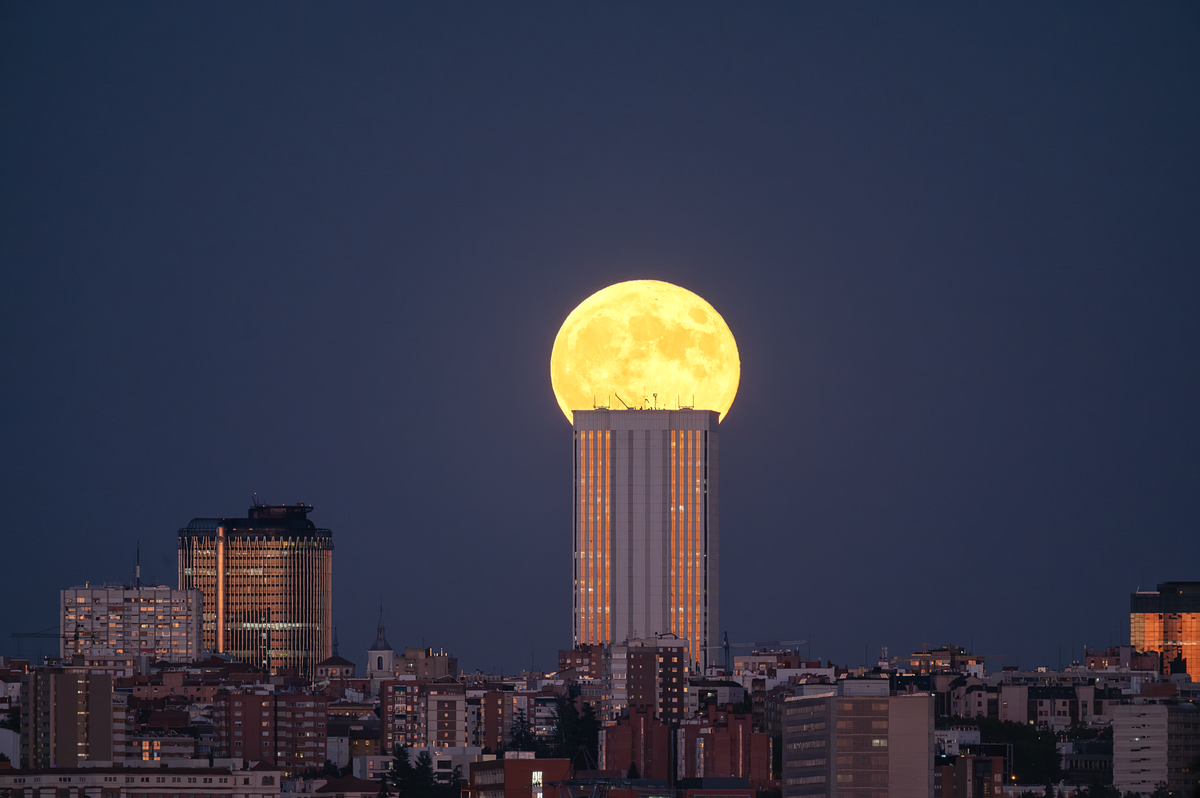 A stunning full moon rising above the Madrid skyline at dusk, when atmospheric refraction creates moon mirages and a flattened appearance