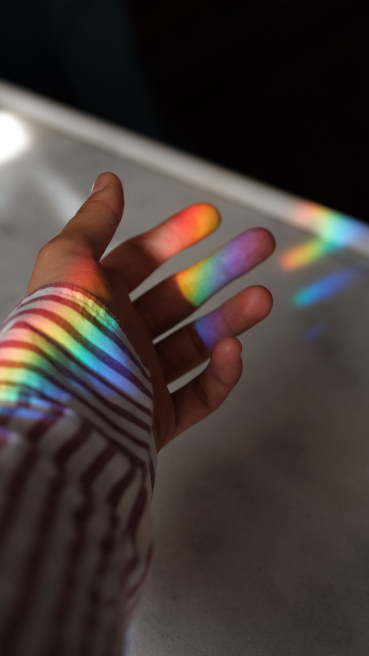 How to make a rainbow: a hand catches a rainbow-coloured light projection from a simple prism experiment