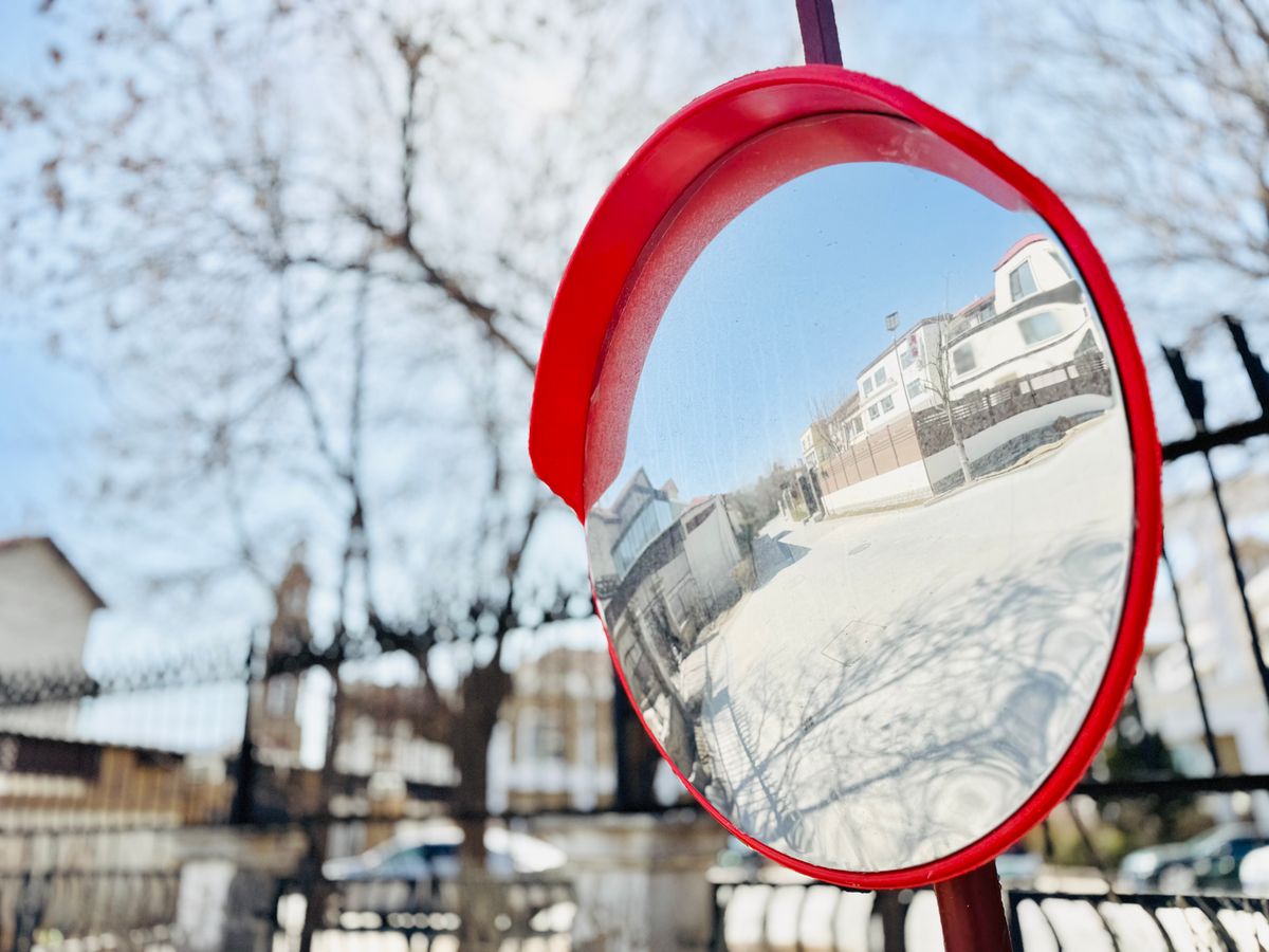 A convex street safety mirror mounted on a pole in an urban setting, showing the wide-angle reflected view that characterises diverging mirrors