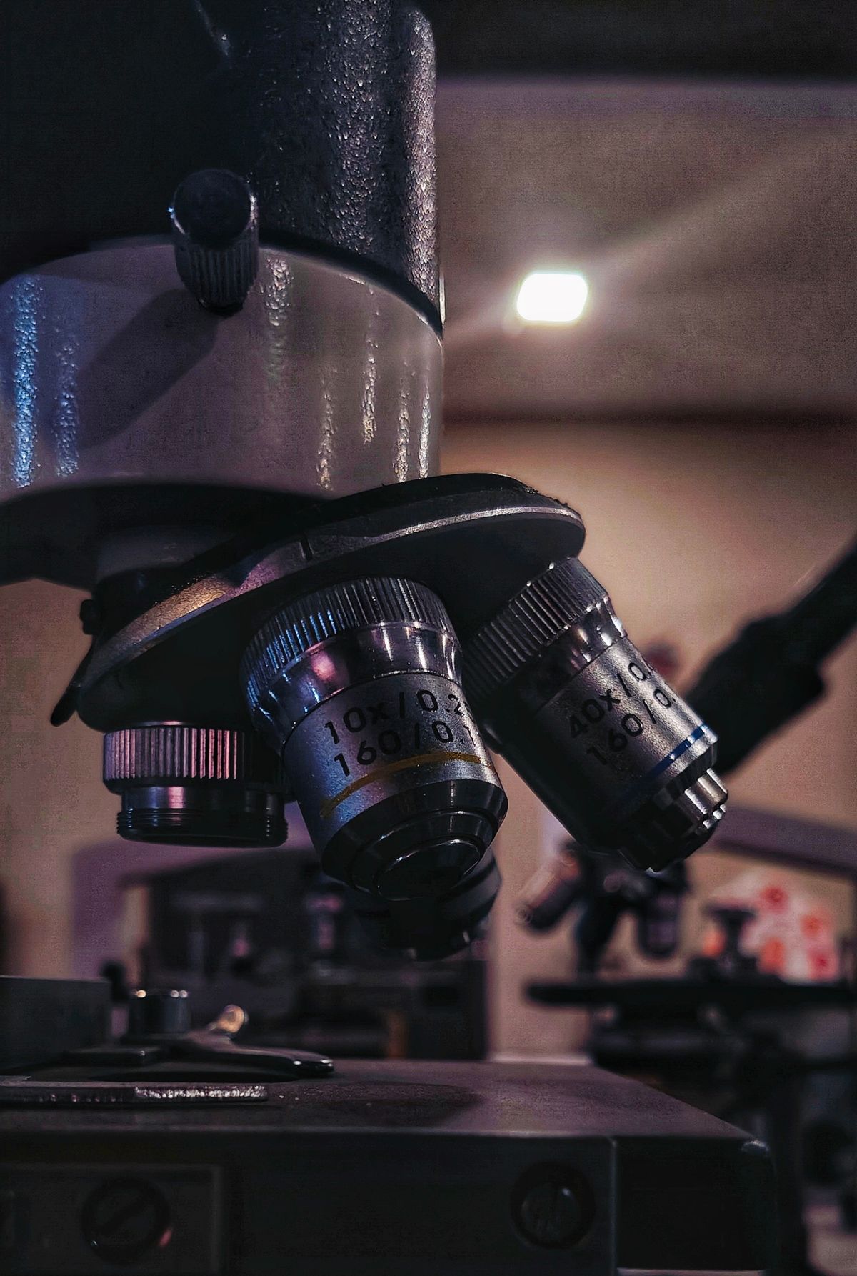 Detailed view of microscope lenses in a dimly lit laboratory setting, similar to the precision optics used in concave mirror experiments
