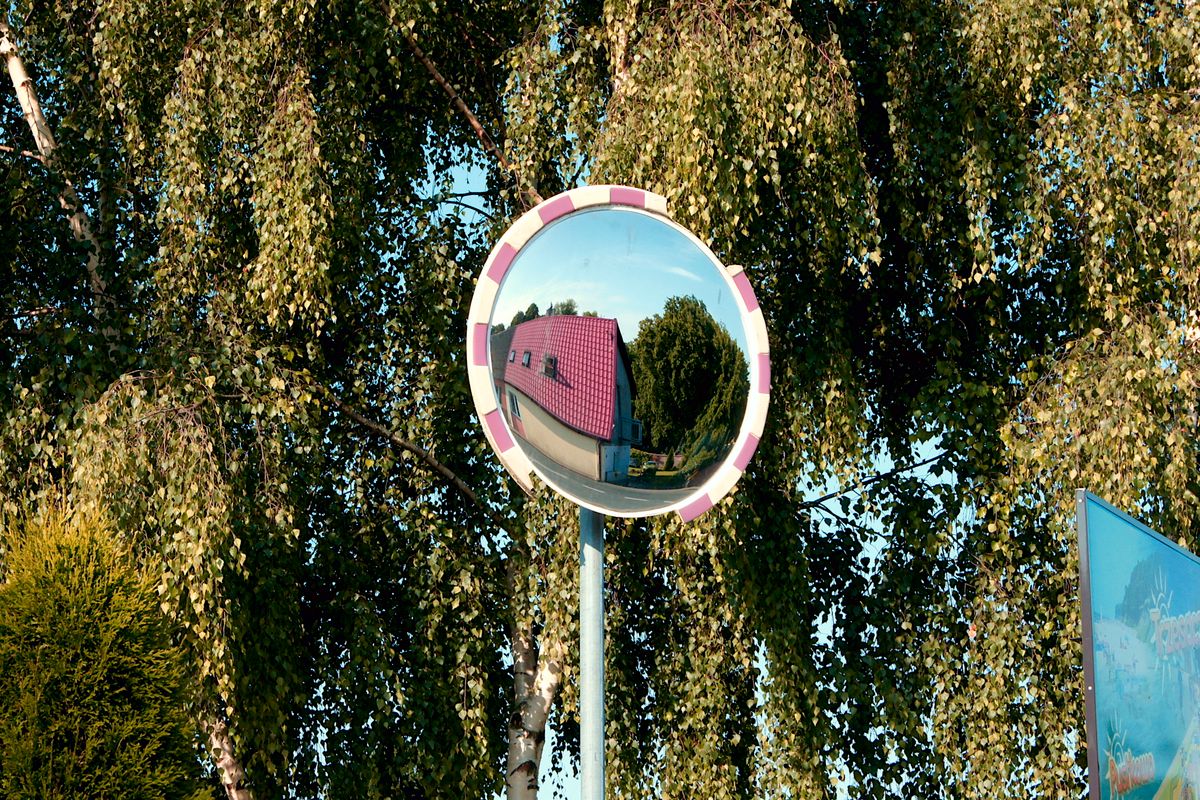 Concave vs convex mirror comparison shown by a convex traffic mirror curving outward to reflect a building and trees over a wide field of view