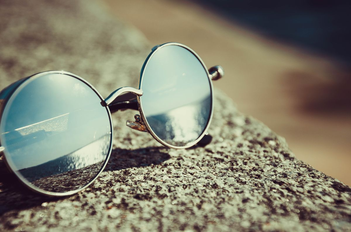 Round sunglasses resting on a sandy beach reflecting the ocean view, demonstrating polarized lens glare reduction