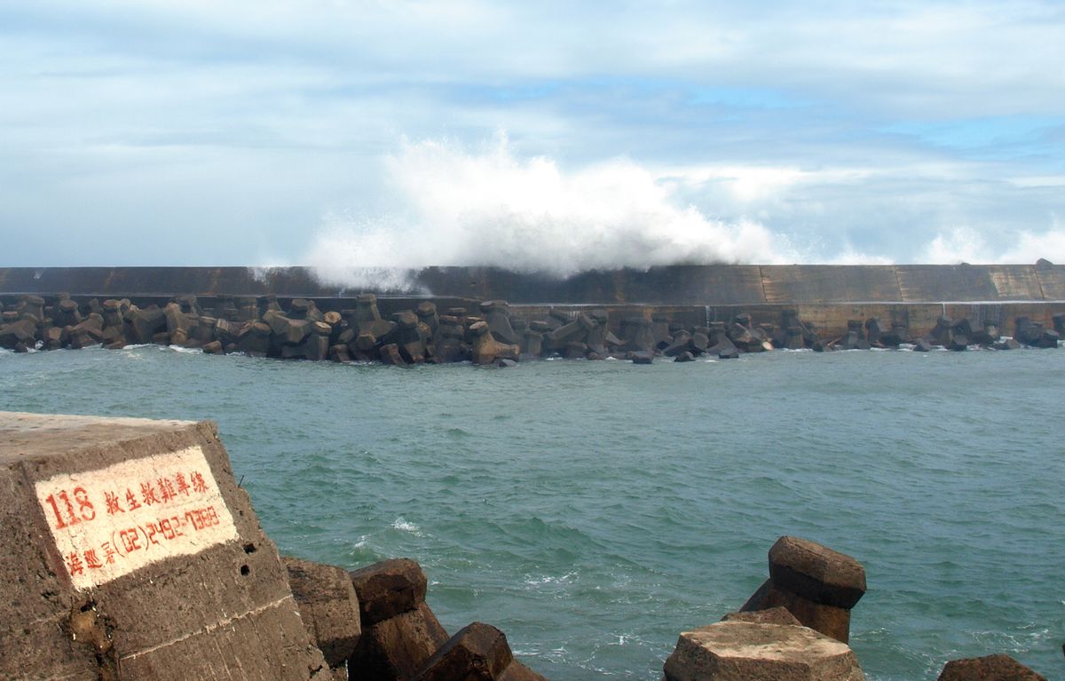 Powerful ocean waves crash against a harbour wall, demonstrating how water waves diffract around obstacles and spread into sheltered areas
