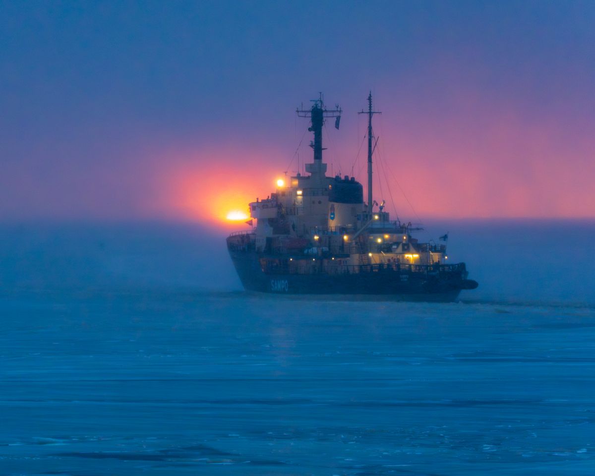 An icebreaker ship cutting through icy Arctic waters at sunset, where temperature inversions create superior mirages that make distant ships appear to float