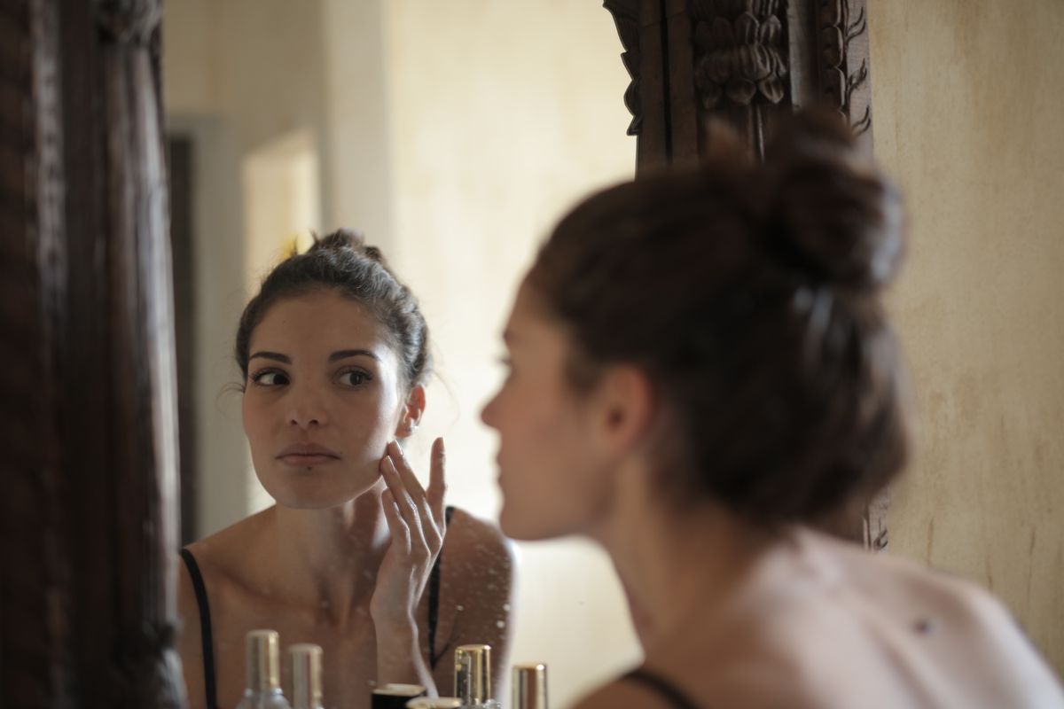 A woman checking her skin in a bathroom mirror, demonstrating everyday reflection of light on a smooth surface