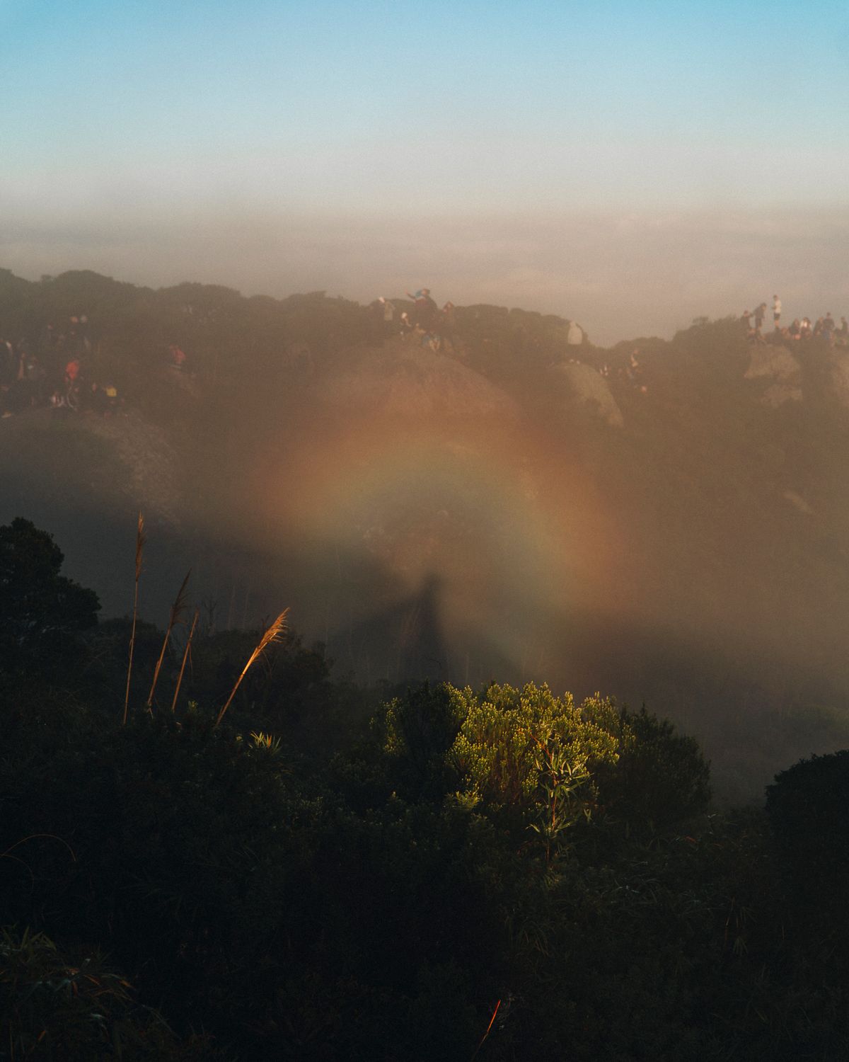 A scenic view above clouds with a pale rainbow arc over misty mountains — a fogbow or white rainbow