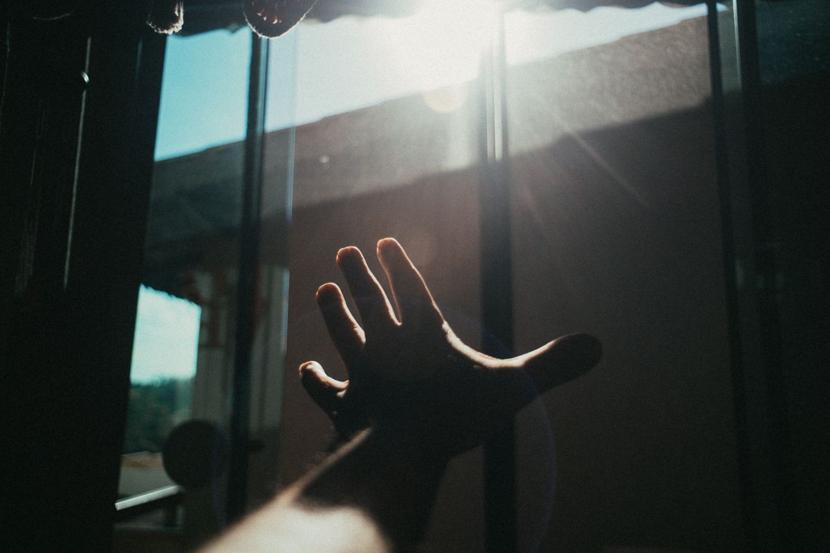 A hand reaching into bright sunlight, feeling light's energy without mass