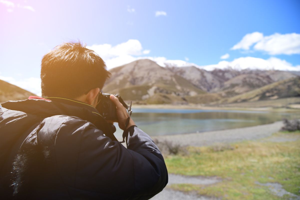 A photographer capturing a scenic mountain lake landscape at sunset, demonstrating outdoor polarizing filter use in landscape photography