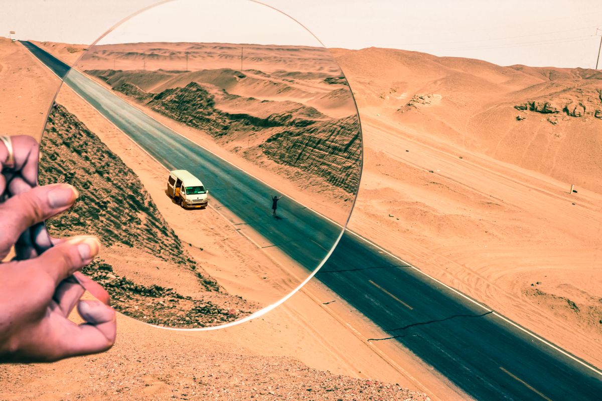 A van travelling on a desert road viewed through a magnifying glass, illustrating how refraction distorts the view in an inferior mirage