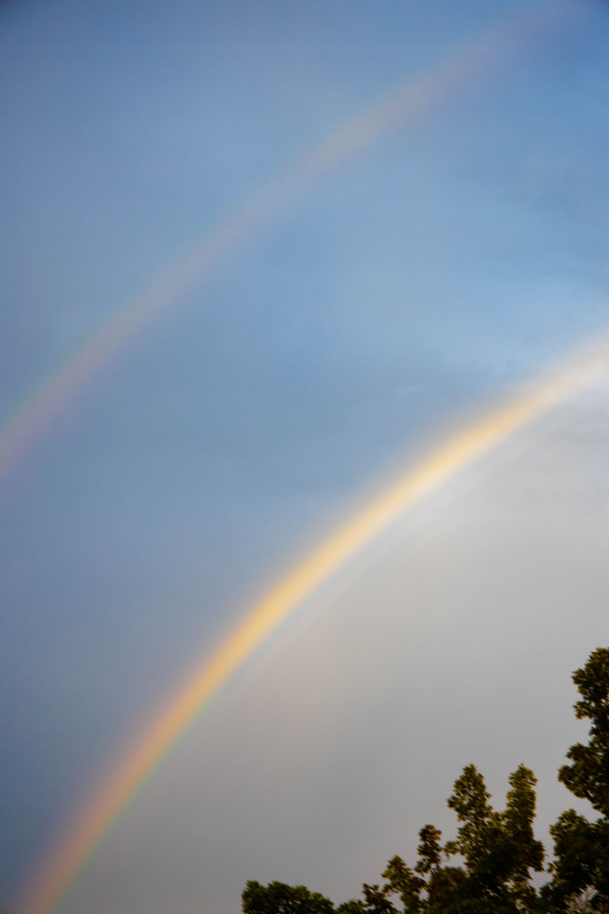 Stunning double rainbow arcs across a blue sky with wispy clouds, demonstrating what causes a double rainbow in nature