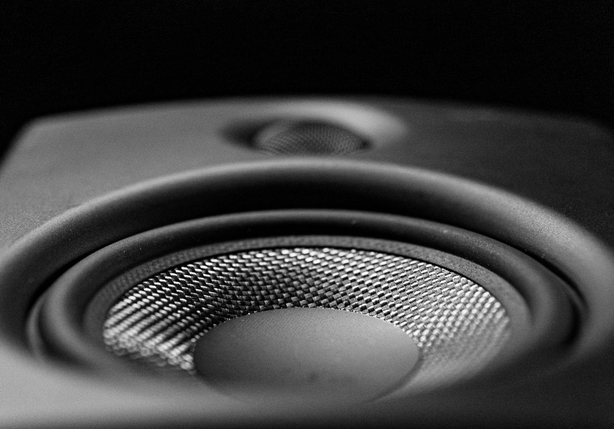 A detailed black-and-white close-up image of a speaker cone, representing sound wave diffraction around obstacles like edges and corners