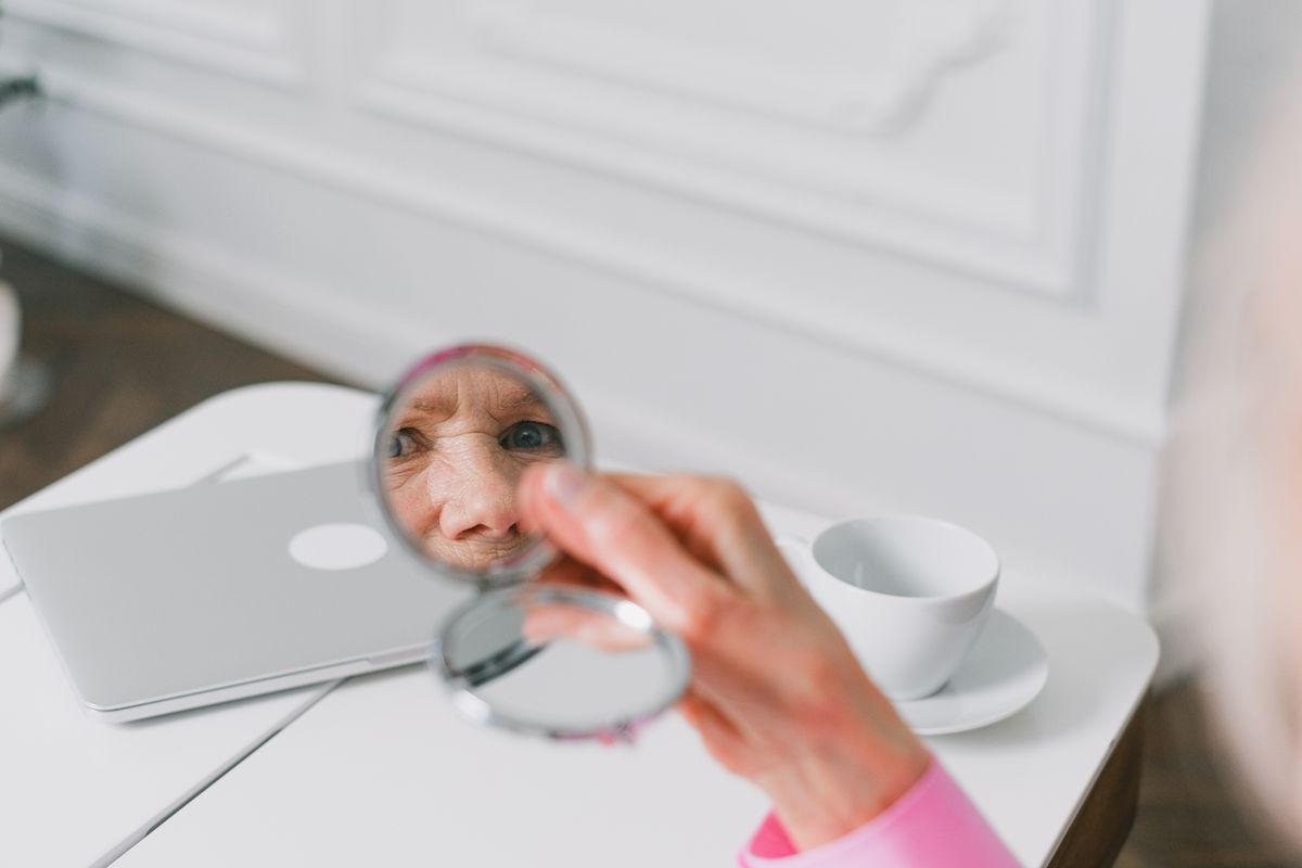 Close-up of a senior woman holding a pocket mirror, showing how specular reflection physics waves create a clear reflected image