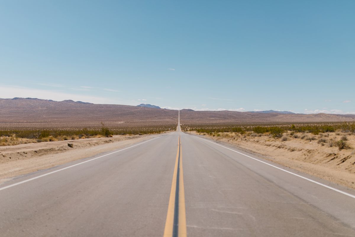 A mirage on road forms where a long, straight desert highway shimmers towards the hot horizon