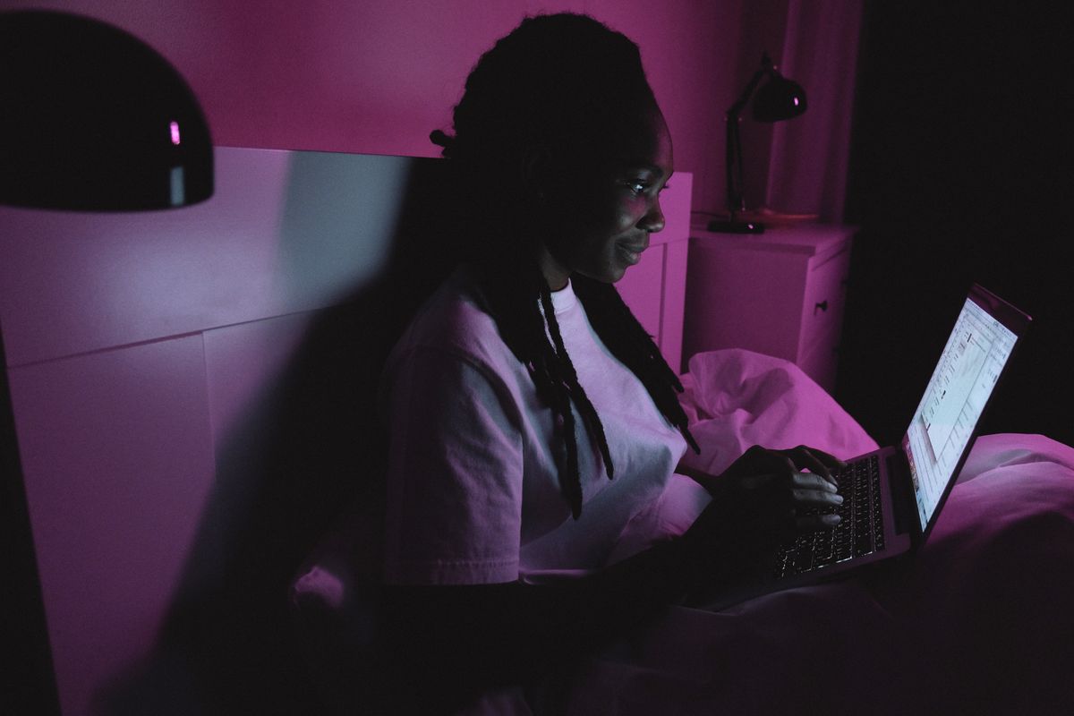 A person on a laptop in bed lit by blue screen light, a source blue light glasses target