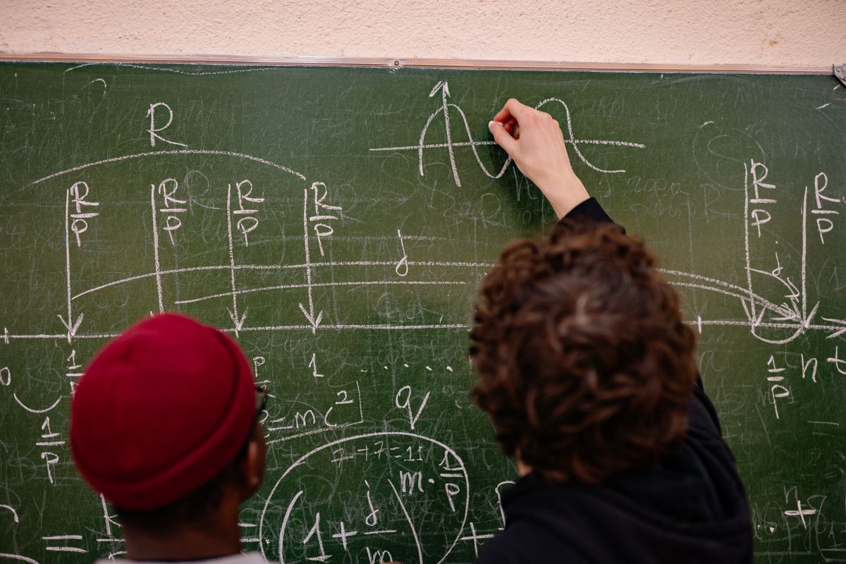 Students working on complex physics equations and diagrams on a chalkboard, illustrating the educational context for learning convex lens ray diagrams