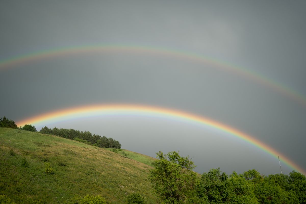 A stunning double rainbow arching over lush green hills in Altai, showing the primary and secondary bows