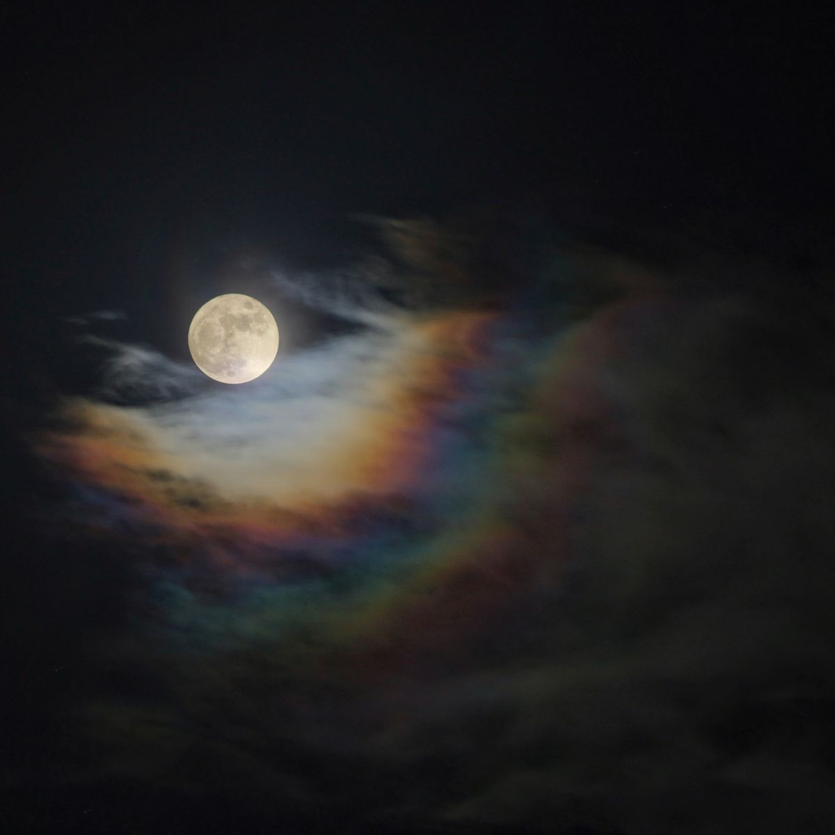A bright full moon illuminating iridescent clouds in a dark night sky — moonlight is the essential ingredient for a moonbow