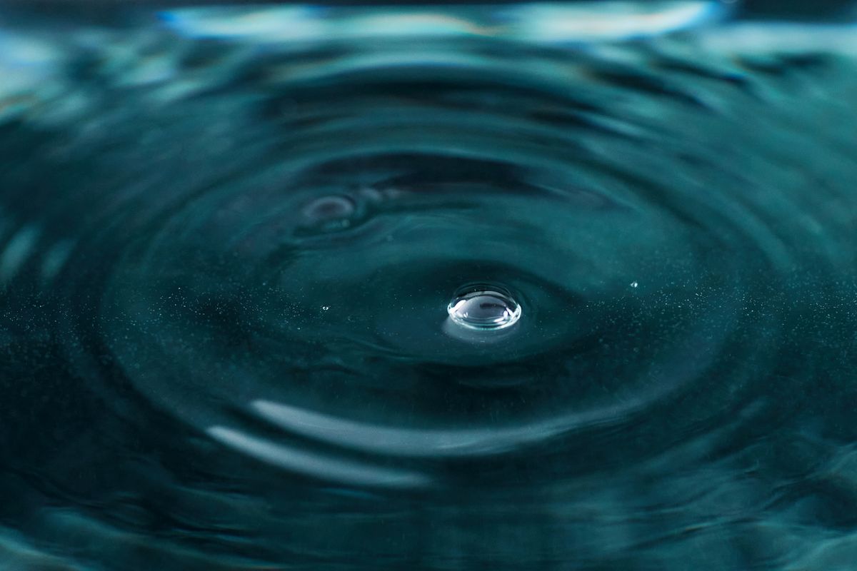 Water droplet creating circular ripples that spread and interact with other wave patterns